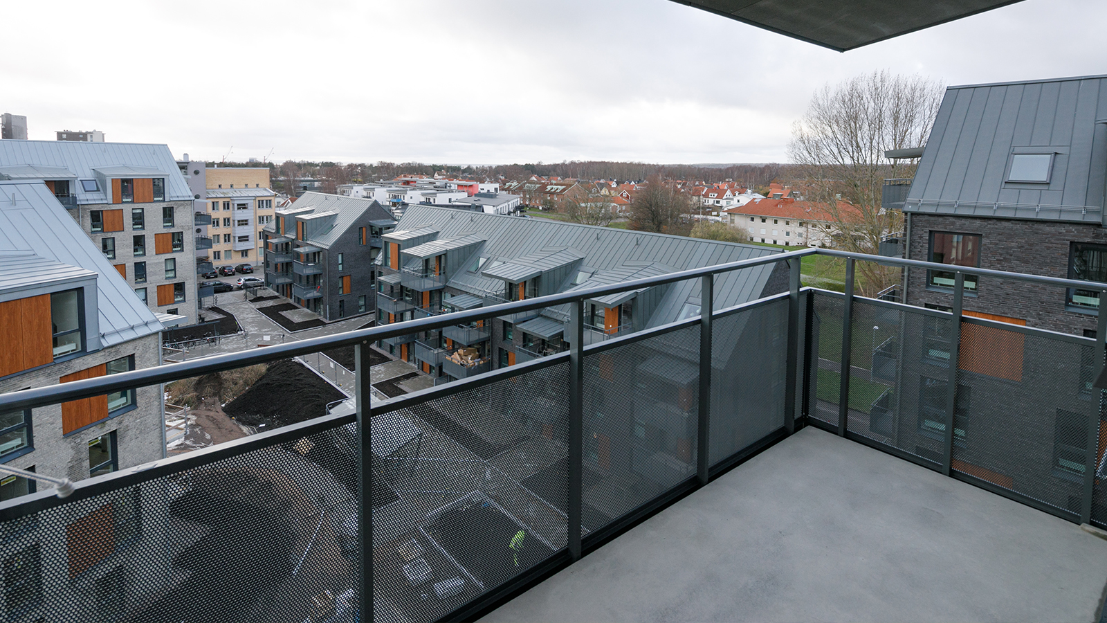 Söder. Utsikt över takåsar och flervåningshus. Flervåningshusen är i modern design, i mörkgrått och beige tegel med partier av blankbrunt trä