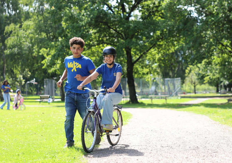 Pojke springer bredvid en tjej som cyklar.
