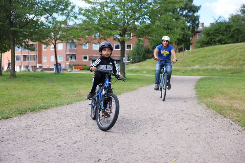 Två killar cyklar på en grusväg i en park.