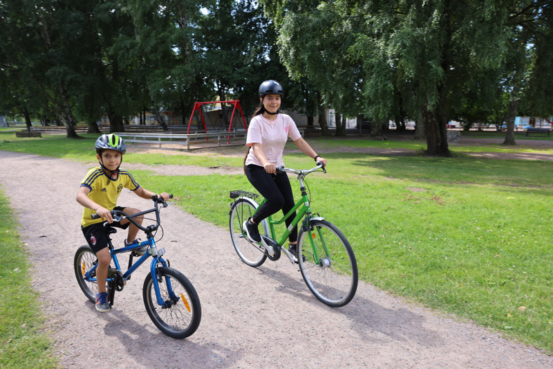 En kille och en tjej cyklar tillsammans i en park.