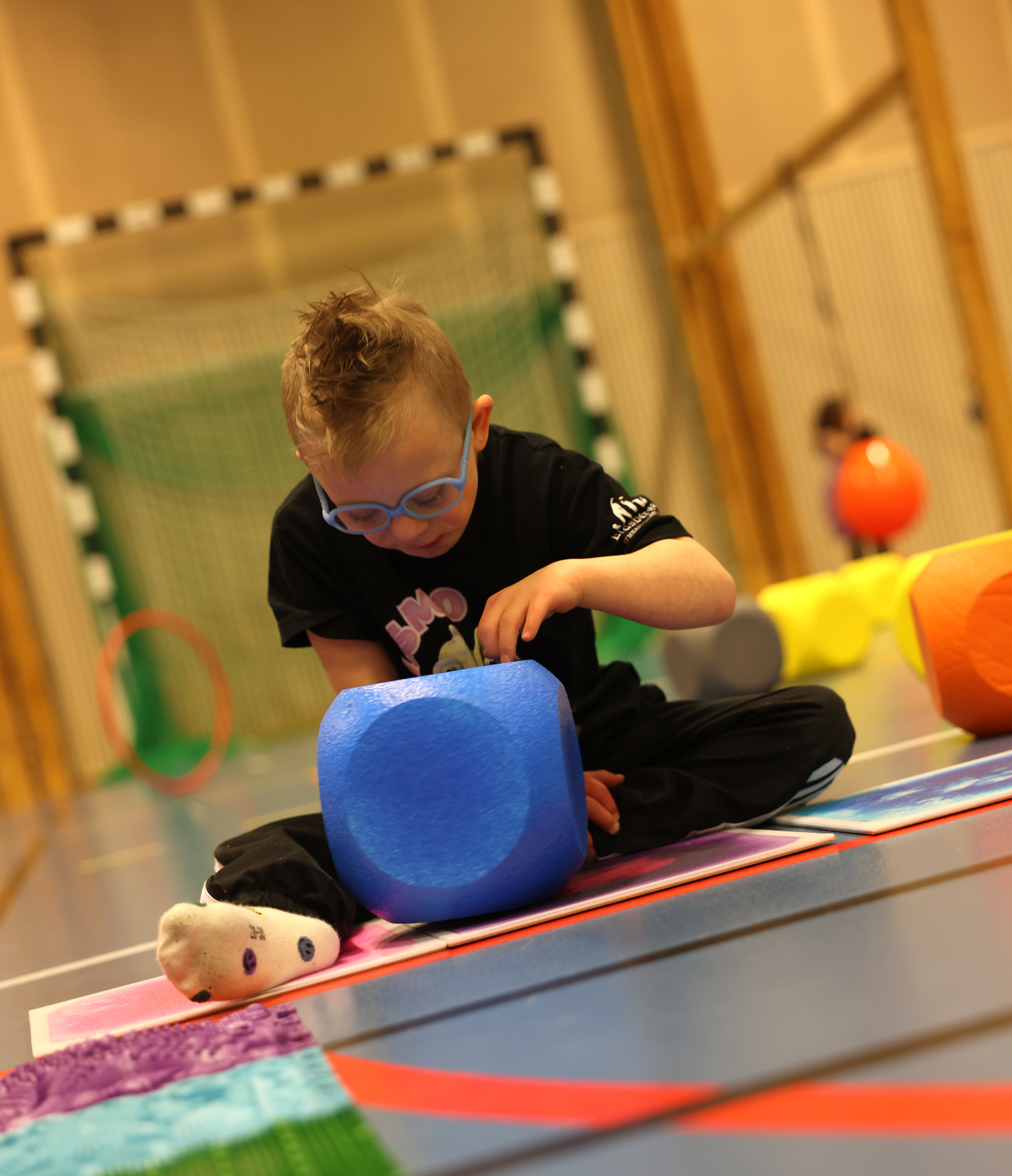 En ung pojke sitter på en matta och leker med ett gosedjur.