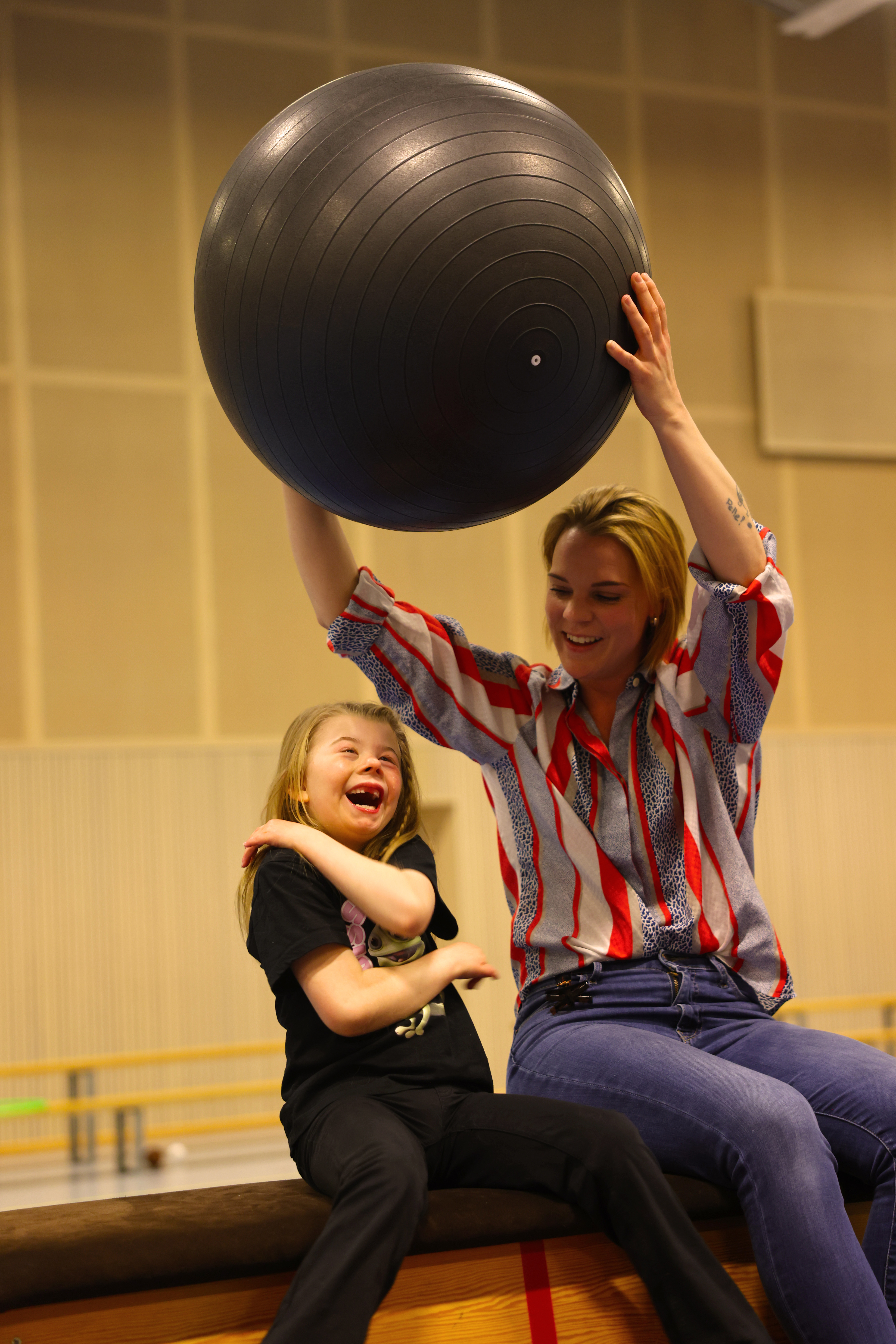 Flicka och vuxen kvinna som leker med en svart yogaboll 