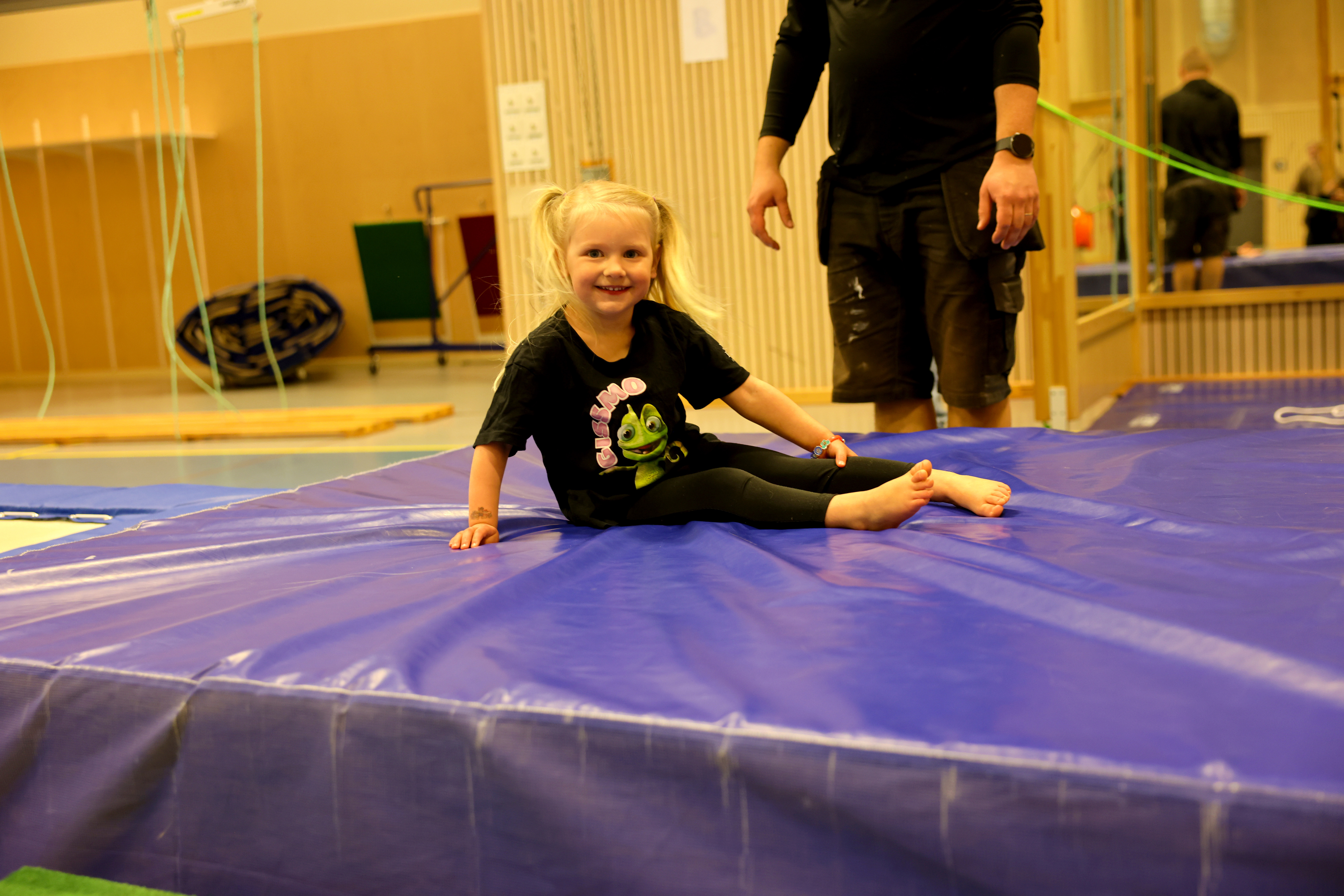 En liten flicka sitter på en trampolin i ett gym.