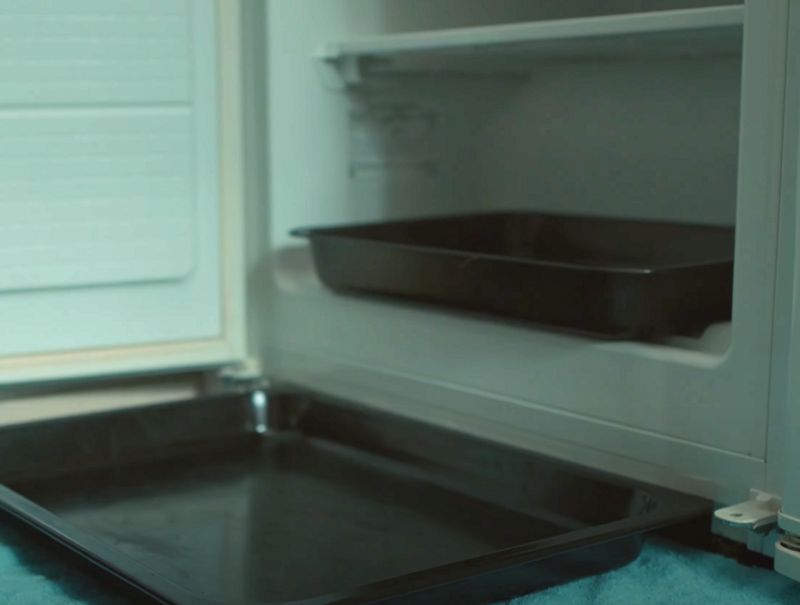 Handduk med bakplåt framför frys som ska frostas av.