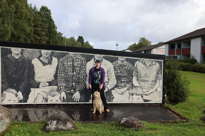 En kvinna och hennes hund som står framför en väggmålning.