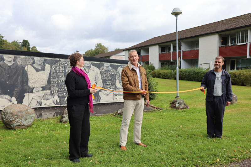 En grupp människor som håller i ett band framför en byggnad.