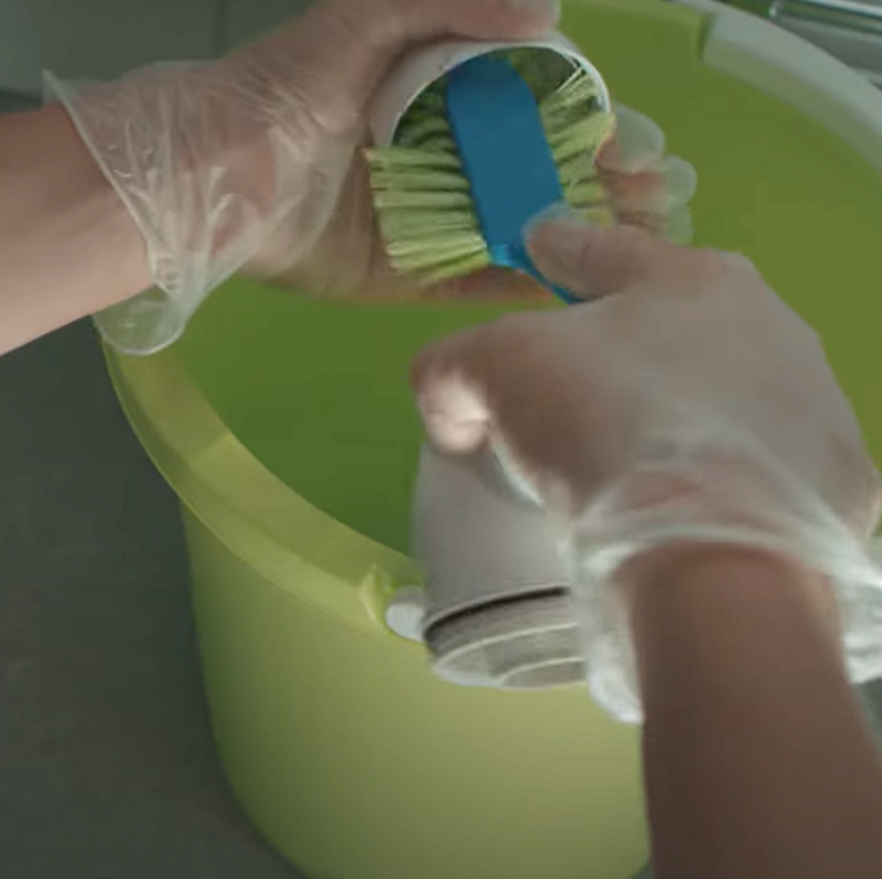 Händer som diskar delar till ett vattenlås i en grön hink. 