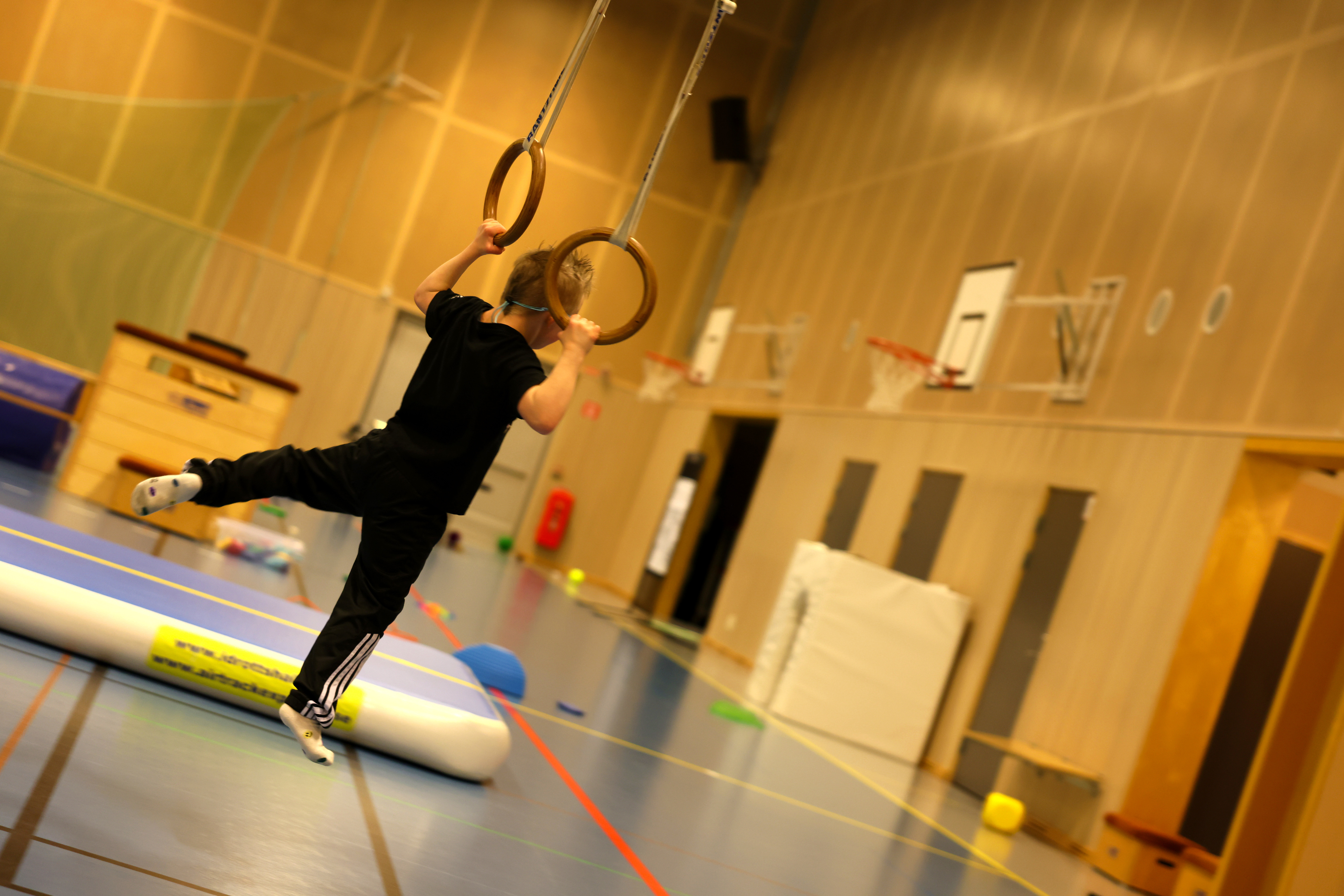 En ung pojke svingar sig i ett rep i ett gym.