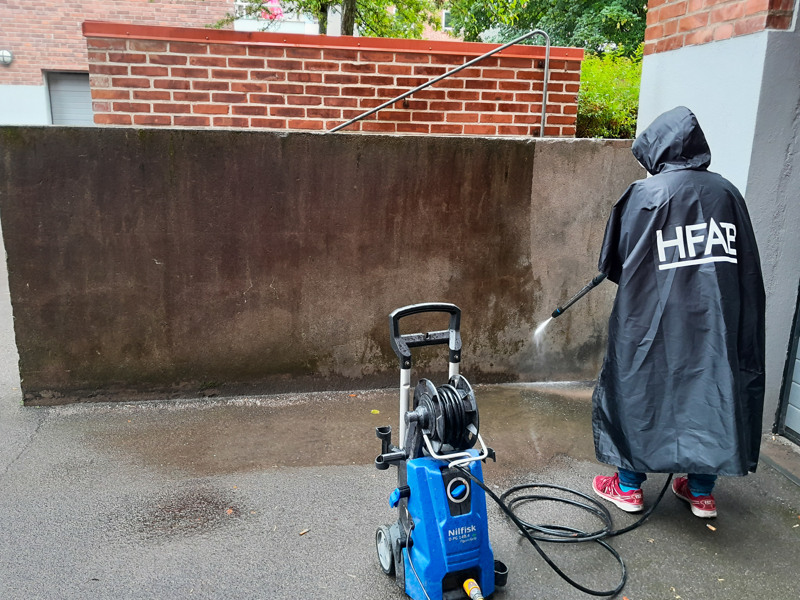 En person i regnrock som använder en högtryckstvätt