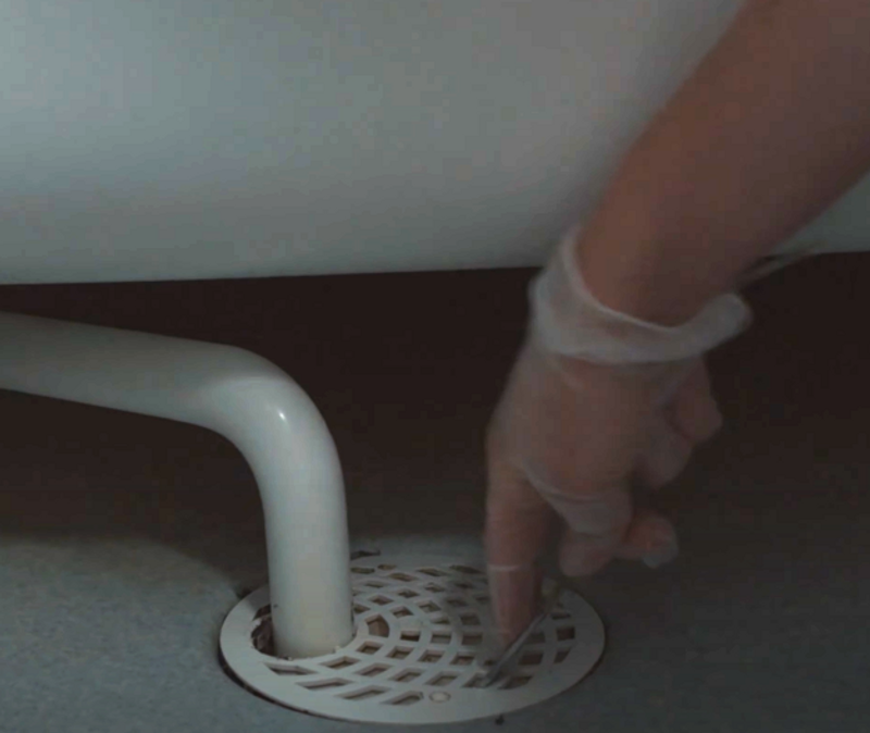 En hand tar upp gallret i golvbrunnen med hjälp av en gaffel.