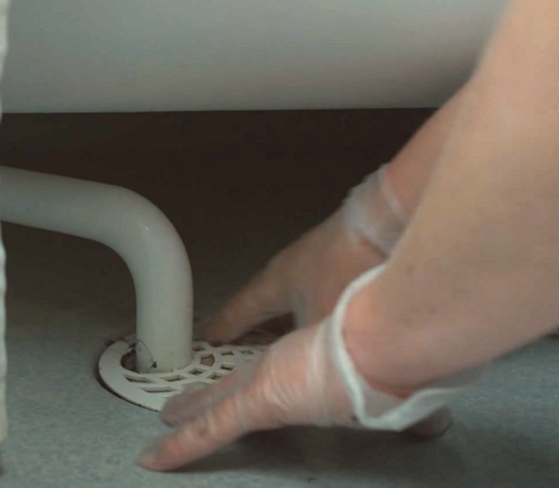 En person sätter tillbaka gallret till en golvbrunn.