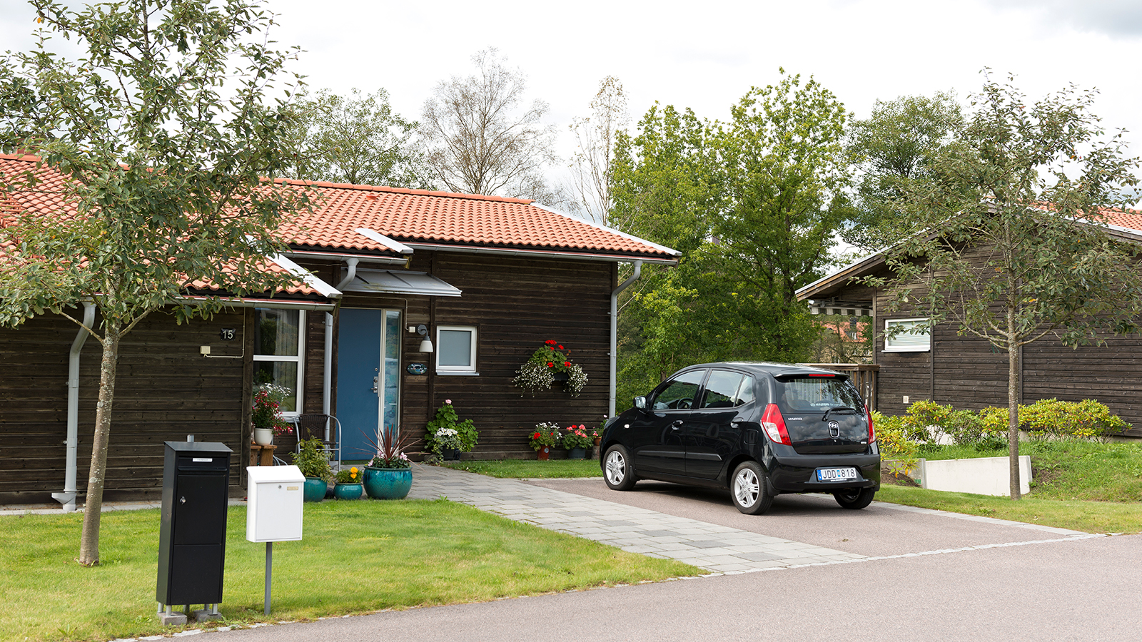 Oskarström. Sommarbild av enplanshus med liggande, brunlaserad träfasad. Till huset hör en egen parkeringsplats.