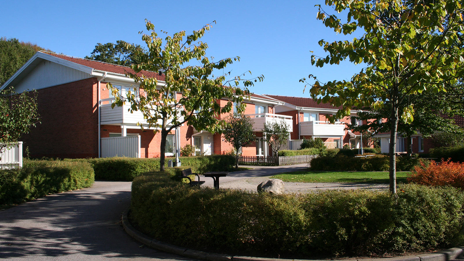 Sofieberg. Höstbild av två flerfamiljshus på vardera två våningar, med rödaktigt tegel, vita träbalkonger och partier med vit träpanel. 